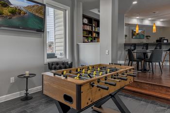 A foosball table is in the middle of a room with a TV and a dining table.